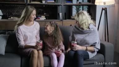 快乐的多代家庭与梅森罐新鲜的浆果冰沙在手中交流，坐在舒适的沙发上